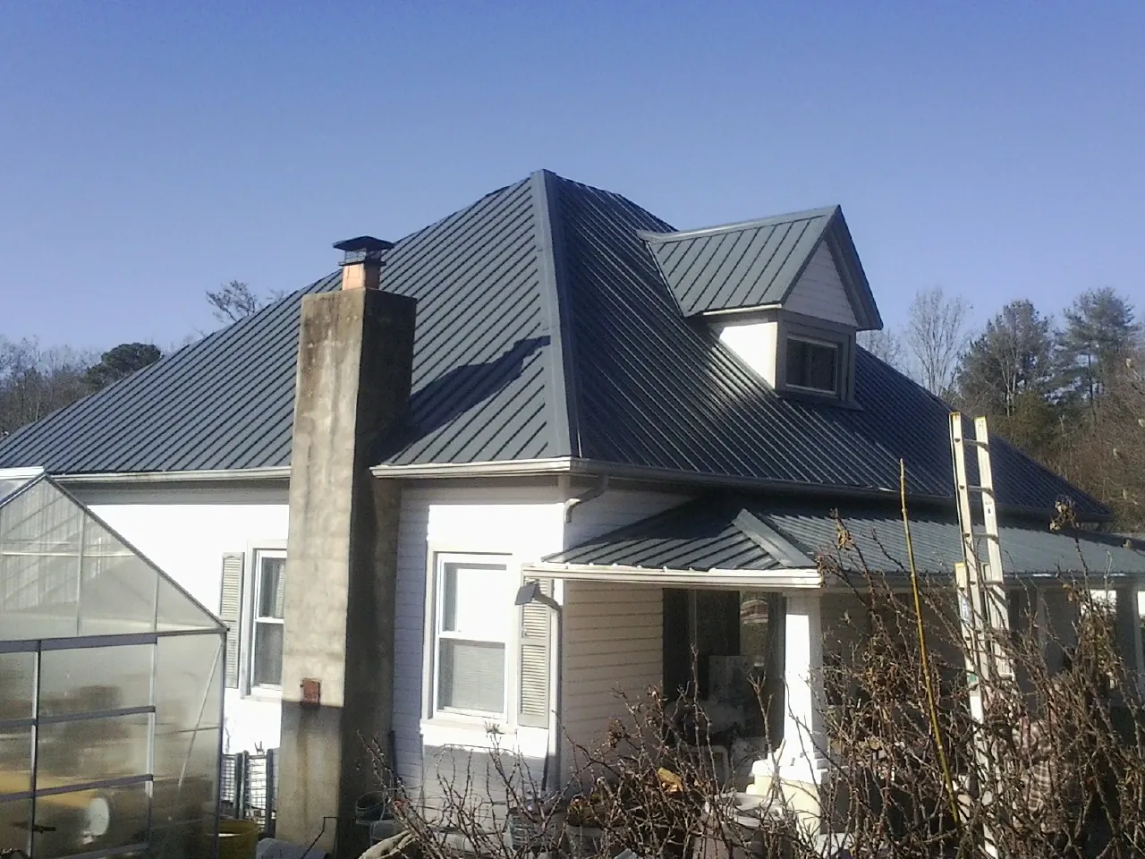 Dark blue standing seam metal roof on a white farmhouse with dormer — Slate & Tile Roof Repair by Roofing Brothers in Panorama City