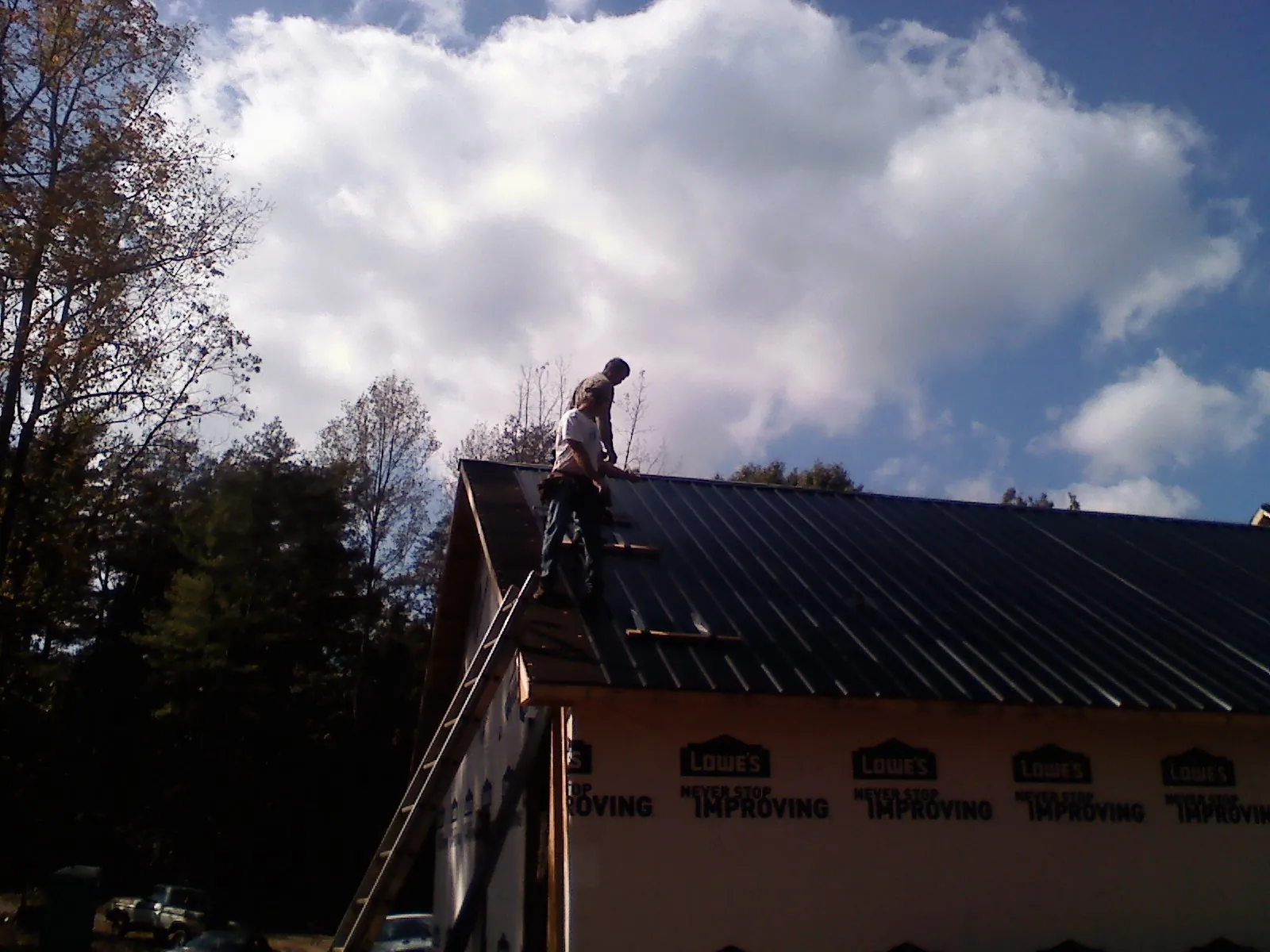 Roofer fastening dark metal panels high against a cloudy sky, from a Roof Inspection job in Panorama City