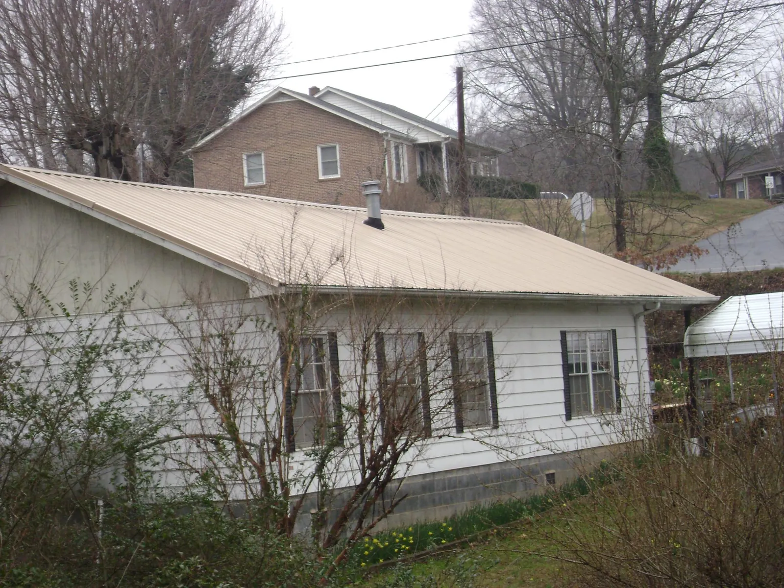 Tan metal roof on a white sided house set into a hillside — Commercial Roofing by Roofing Brothers in Panorama City